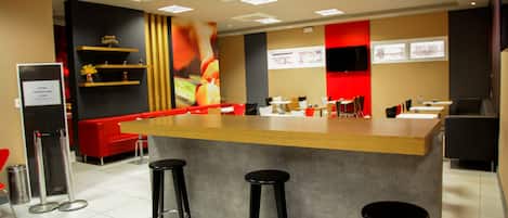 A modern restaurant interior with a central bar, red seating, and a tiled floor.