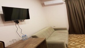 A room with a flat-screen TV mounted on the wall, a sofa, a wooden table with water bottles, and an air conditioning unit. - Classic Hotel Tbilisi (Tbilisi)