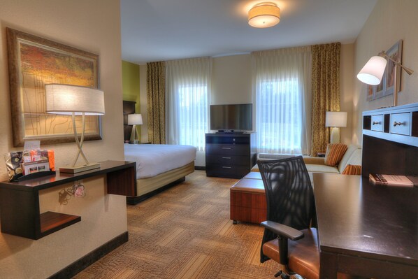 A hotel room with a bed, desk, chair, TV, and a reception desk.