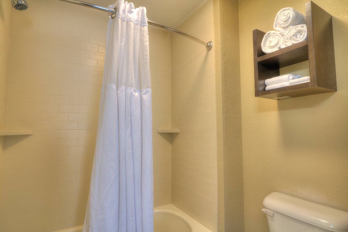 A bathroom with a shower curtain, a bathtub, a toilet, and a shelf with towels.