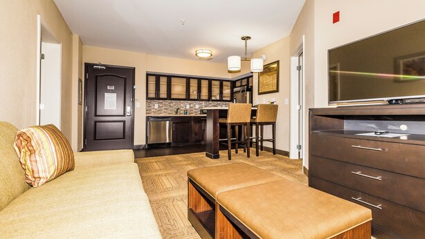 A modern kitchen with dark cabinets, a stainless steel refrigerator, and a large flat-screen TV. - Staybridge Suites Knoxville-West by IHG (Farragut)