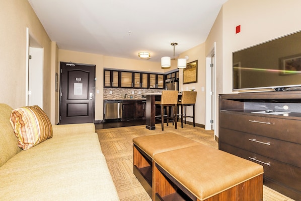 A modern kitchen with dark cabinets, a stainless steel refrigerator, and a large flat-screen TV. - Staybridge Suites Knoxville-West by IHG (Farragut)