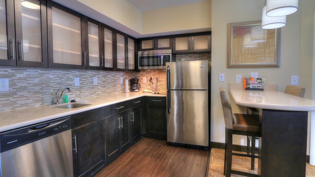 A modern kitchen with dark cabinets, stainless steel appliances, a dishwasher, and a bar area with a chair. - Staybridge Suites Knoxville-West by IHG (Farragut)