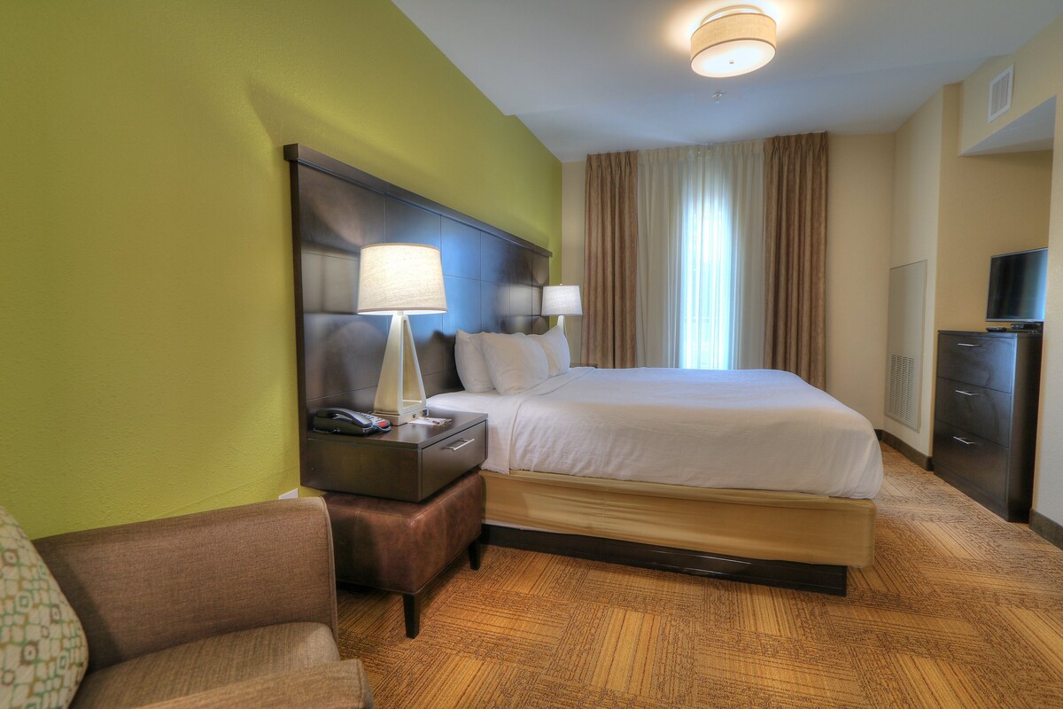 Une chambre d’hôtel avec un grand lit, deux lampes de chevet, une table de nuit, un téléviseur et un fauteuil en cuir marron.