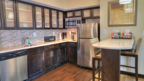A modern kitchen with dark wooden cabinets, stainless steel appliances, a built-in microwave, and a small dining area with a bar stool. - Staybridge Suites Knoxville-West by IHG (Farragut)