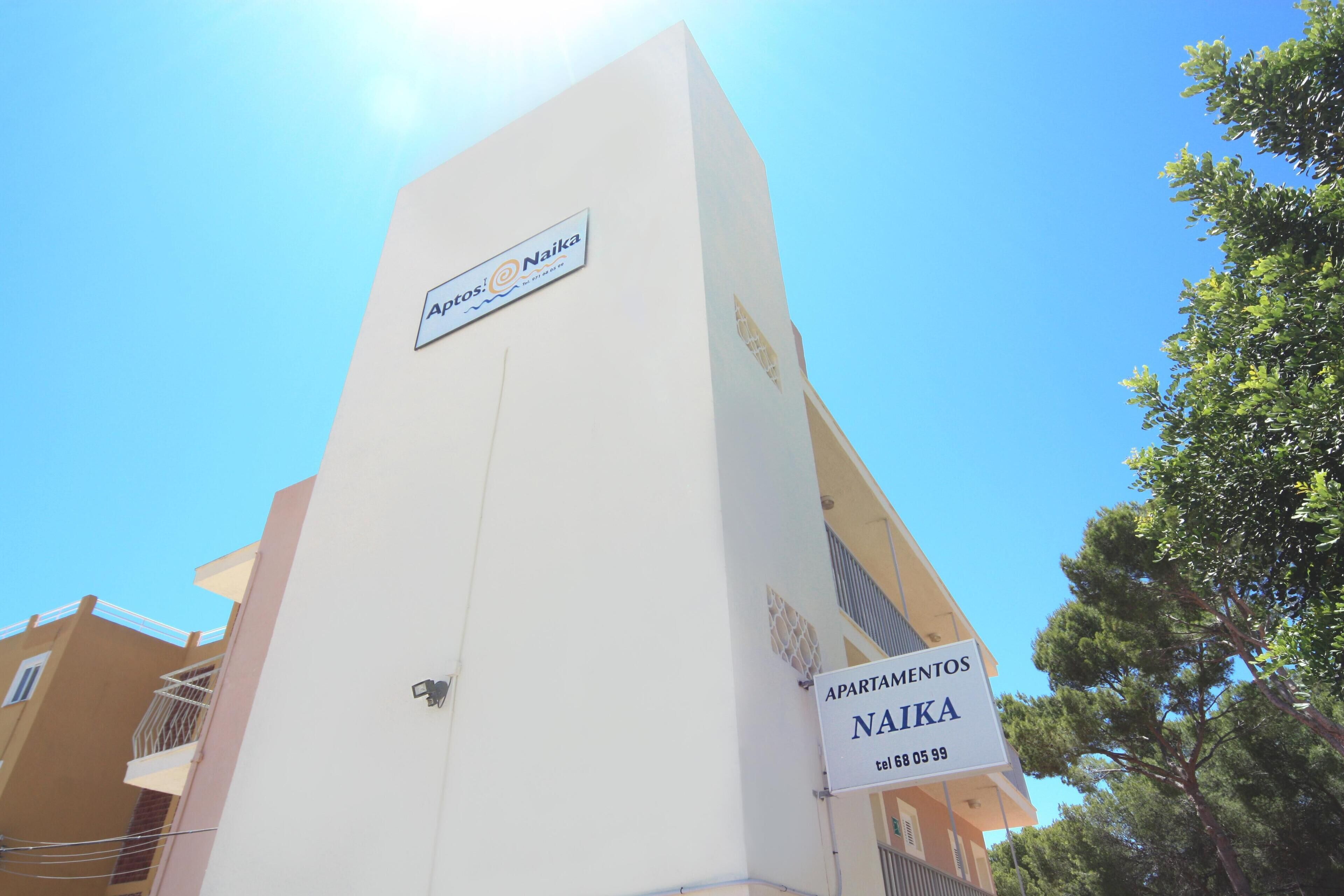 A building with a sign reading "APARTAMENTOS NAIKA" and a contact number.