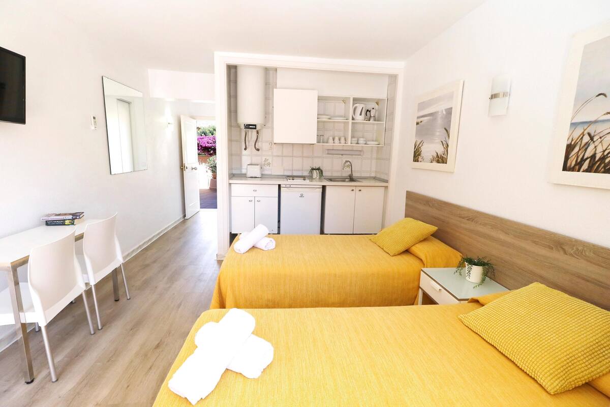 A hotel room with two beds, a kitchenette, a dining area, and a bathroom.