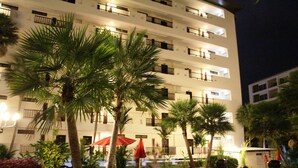 A multi-story hotel with balconies, outdoor seating areas with umbrellas, and palm trees.