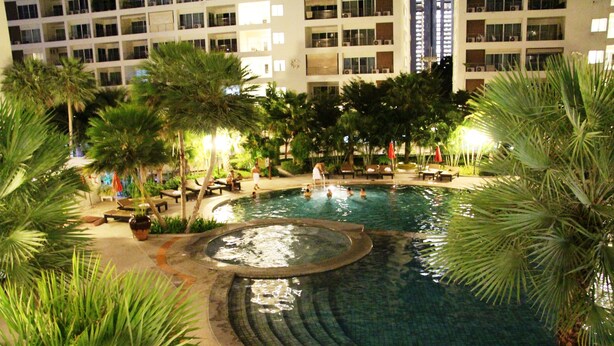 A swimming pool surrounded by palm trees and lounge chairs, with a building in the background.