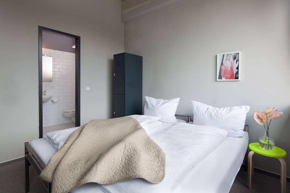 Ein Hotelzimmer mit einem Bett, einem Kleiderschrank, einem kleinen Tisch mit einer Vase und einem gerahmten Bild an der Wand.
