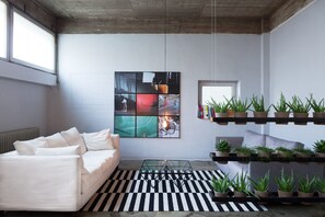 Una sala de estar moderna con un sofá blanco, un tapete a rayas negro y blanco, una mesa de centro de vidrio y un estante para plantas montado en la pared.