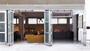 Una entrada abierta a un edificio moderno con un mostrador de recepción visible, un área de descanso con un sofá amarillo y un letrero en la pared que dice “WALL YARD”.