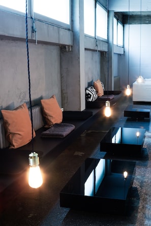 Un área de estar moderna con asientos, iluminación colgante y ventanas amplias.