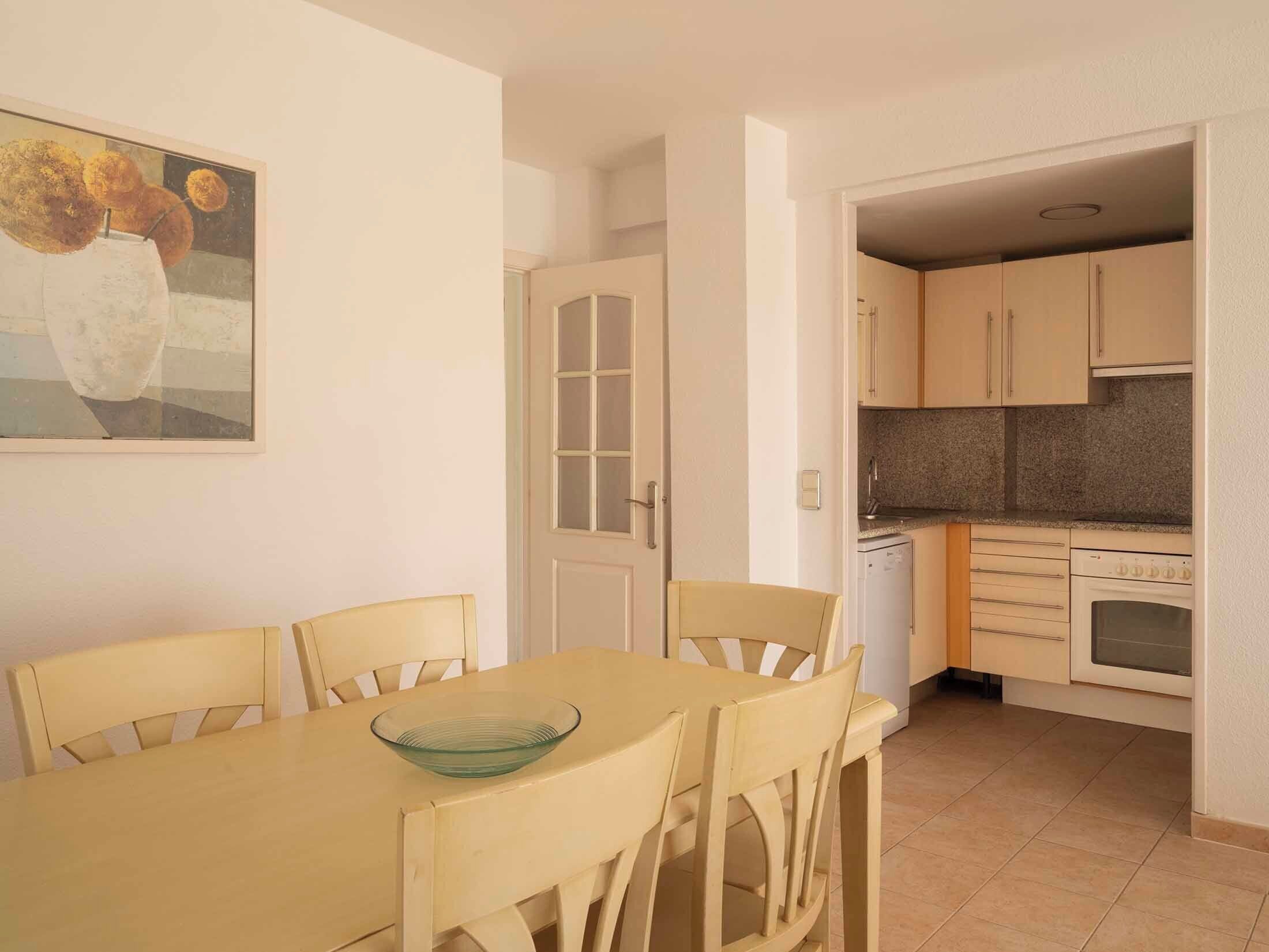 A dining area with a table and chairs, a kitchen with cabinets and appliances, and a door leading to another room.