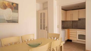 A dining area with a table and chairs, a kitchen with cabinets and appliances, and a door leading to another room.