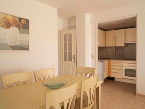 Un comedor con mesa y sillas, una cocina con armarios y electrodomésticos, y una puerta que da a otra habitación.