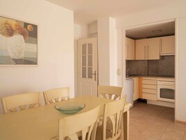 Un comedor con mesa y sillas, una cocina con armarios y electrodomésticos, y una puerta que da a otra habitación.