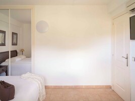 Habitación de hotel con cama, mesita de noche, lámpara, televisor montado en la pared y una puerta.
