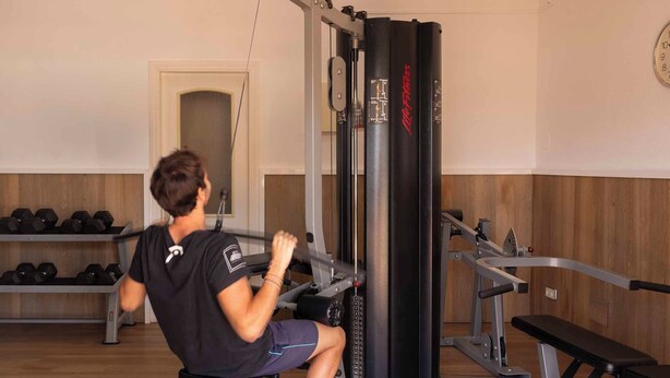 Un gimnasio con una máquina de remo sentado, mancuernas y una estructura para sentadillas.