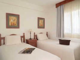 Una habitación de hotel con dos camas individuales, una mesita de noche con lámpara y una ventana con cortinas.
