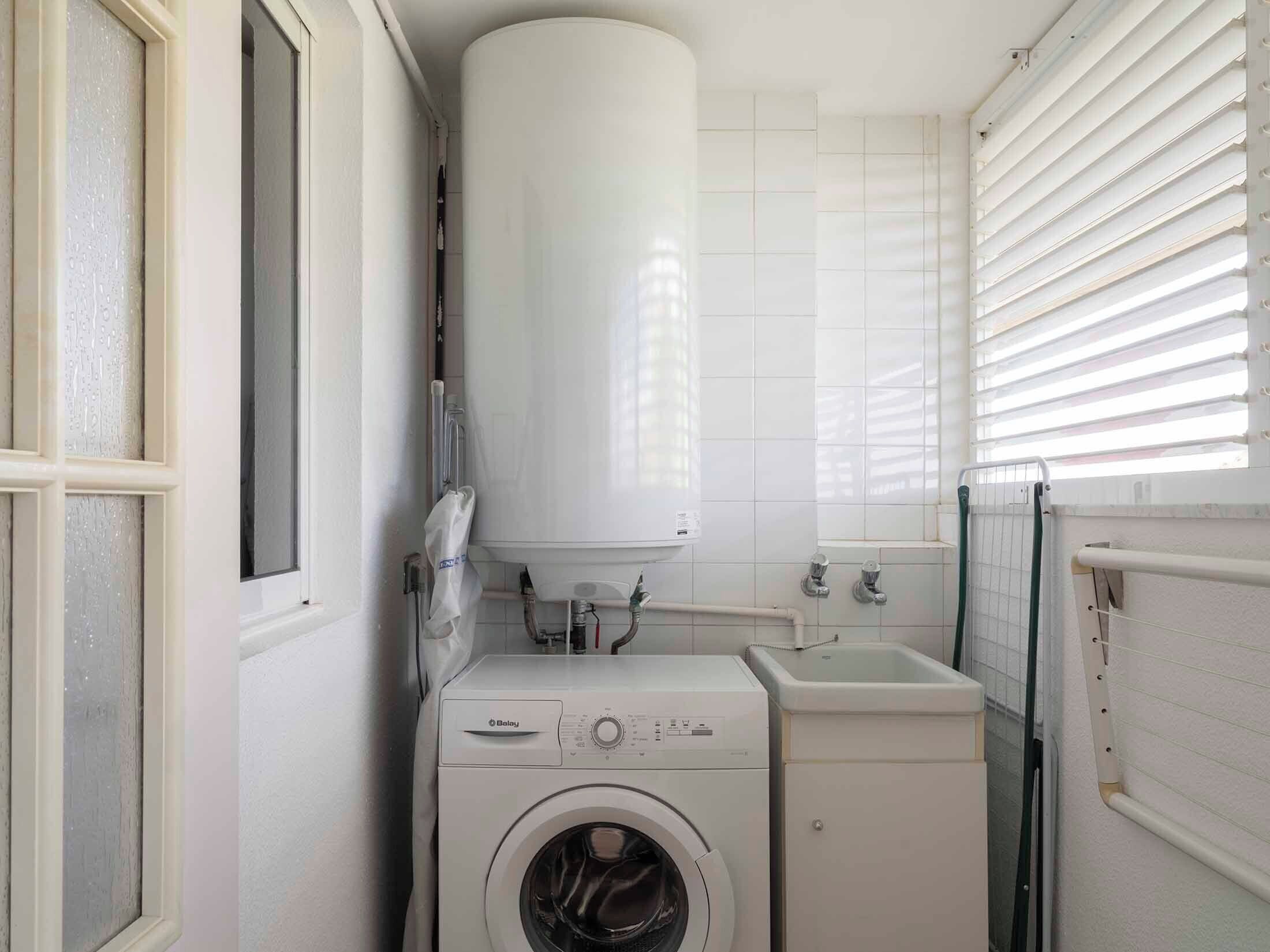 A compact laundry room with a front-loading washing machine, a sink, and a water heater.