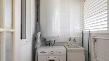 A compact laundry room with a front-loading washing machine, a sink, and a water heater.