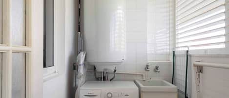 Ein kleiner Hauswirtschaftsraum mit einer Waschmaschine mit Frontlader, einem Waschbecken und einem Warmwasserbereiter.