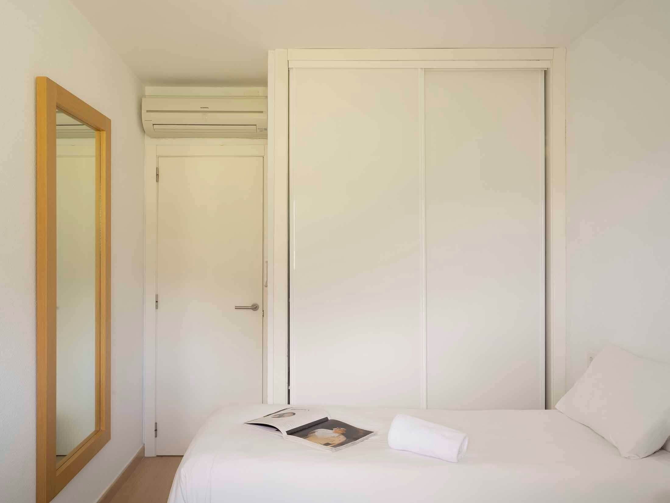A bedroom with a bed, a bedside table, a mirror, and a wardrobe.