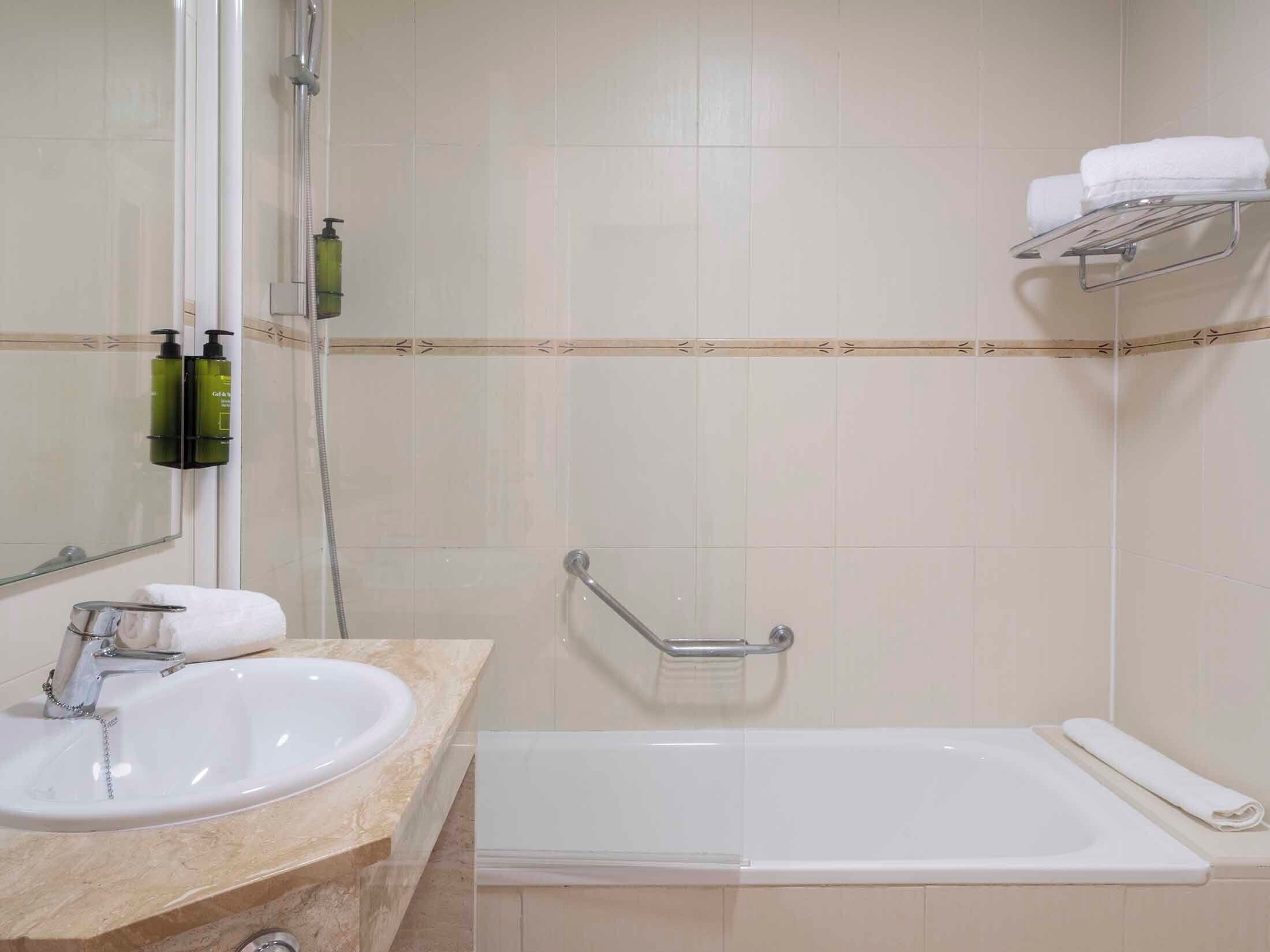 Baño con lavamanos, espejo, ducha y perchero para toallas.