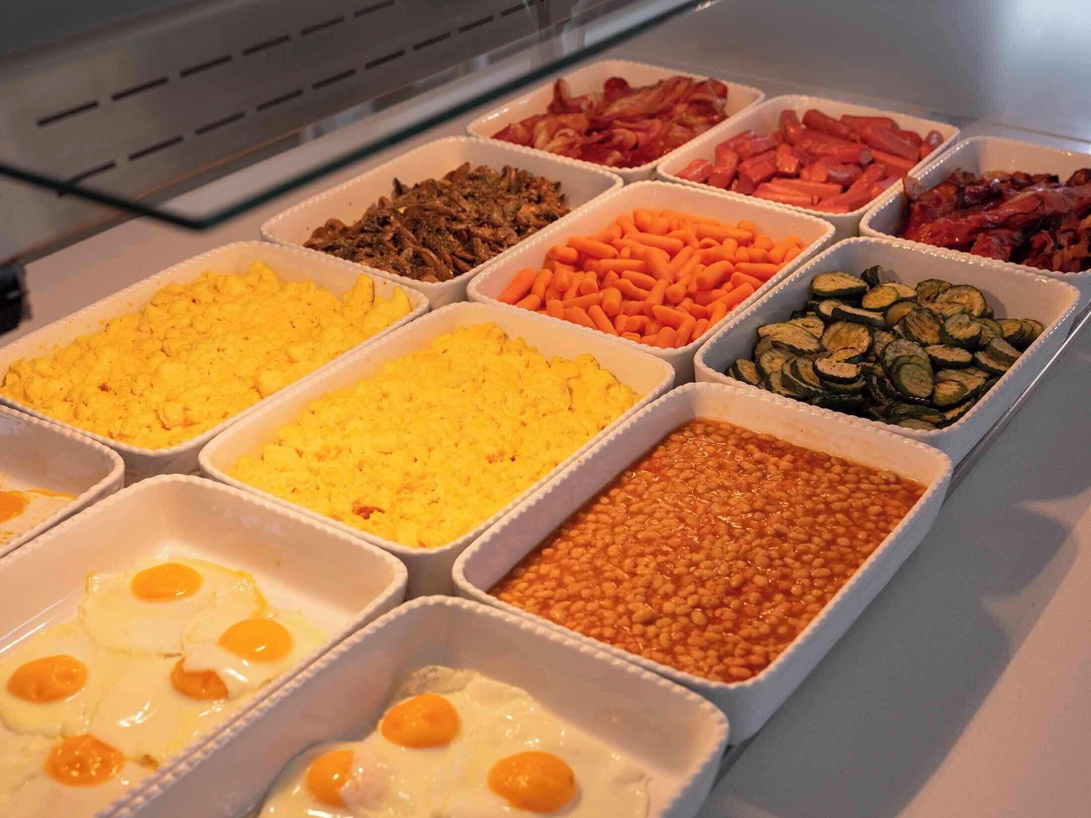 Un bufé con diversas opciones de comida, incluyendo huevos revueltos, tocino, zanahorias y frijoles.