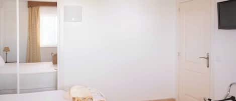 Habitación de hotel con cama, televisor montado en la pared, una puerta y una ventana con cortinas.