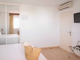Quarto de hotel com uma cama, televisão fixada na parede, porta e janela com cortinas.