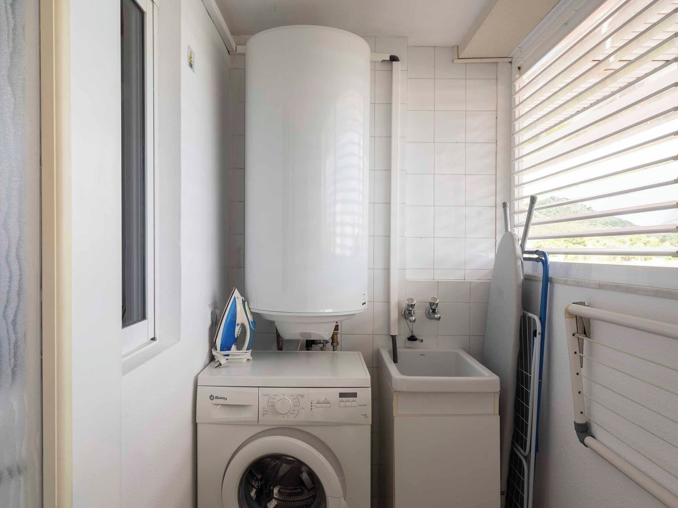 Een kleine wasruimte met een wasmachine, een boiler en een wasbak.
