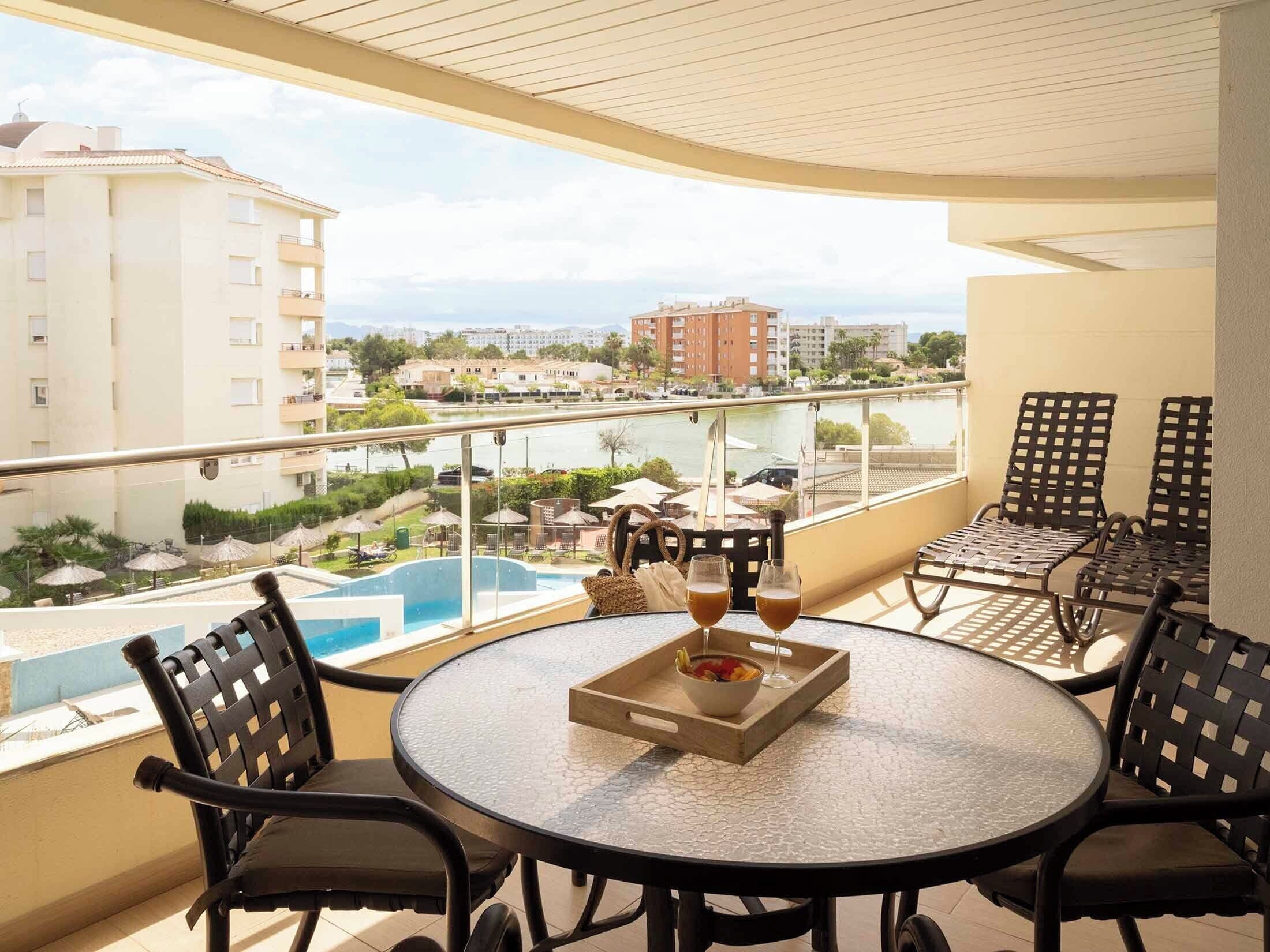 A balcony with a round table, chairs, and a view of a swimming pool and buildings.