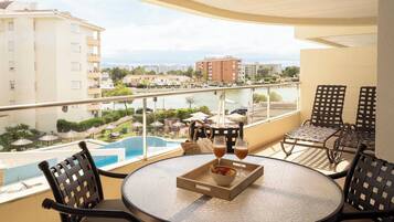 A balcony with a round table, chairs, and a view of a swimming pool and buildings.