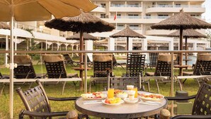 An outdoor dining area with round tables, chairs, and thatched umbrellas. - Ona Garden Lago (Alcúdia)