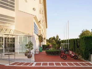 Entrada de hotel con una galería techada, plantas en macetas y un aparcamiento para bicicletas.
