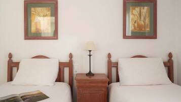 Una habitación de hotel con dos camas, una mesita de noche, una lámpara y dos cuadros en la pared.