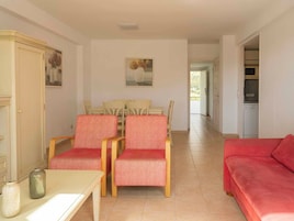 A living room with a dining area, a red sofa, and a kitchen visible through an open door.