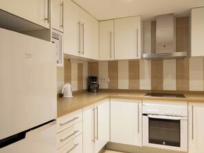 Una cocina moderna con armarios blancos, horno empotrado y cafetera sobre la encimera.