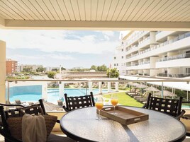 Un balcón con piscina, sillones de descanso y una mesa con bebidas.