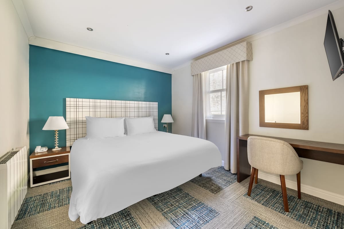 A hotel room with a large bed, a desk, and a chair.