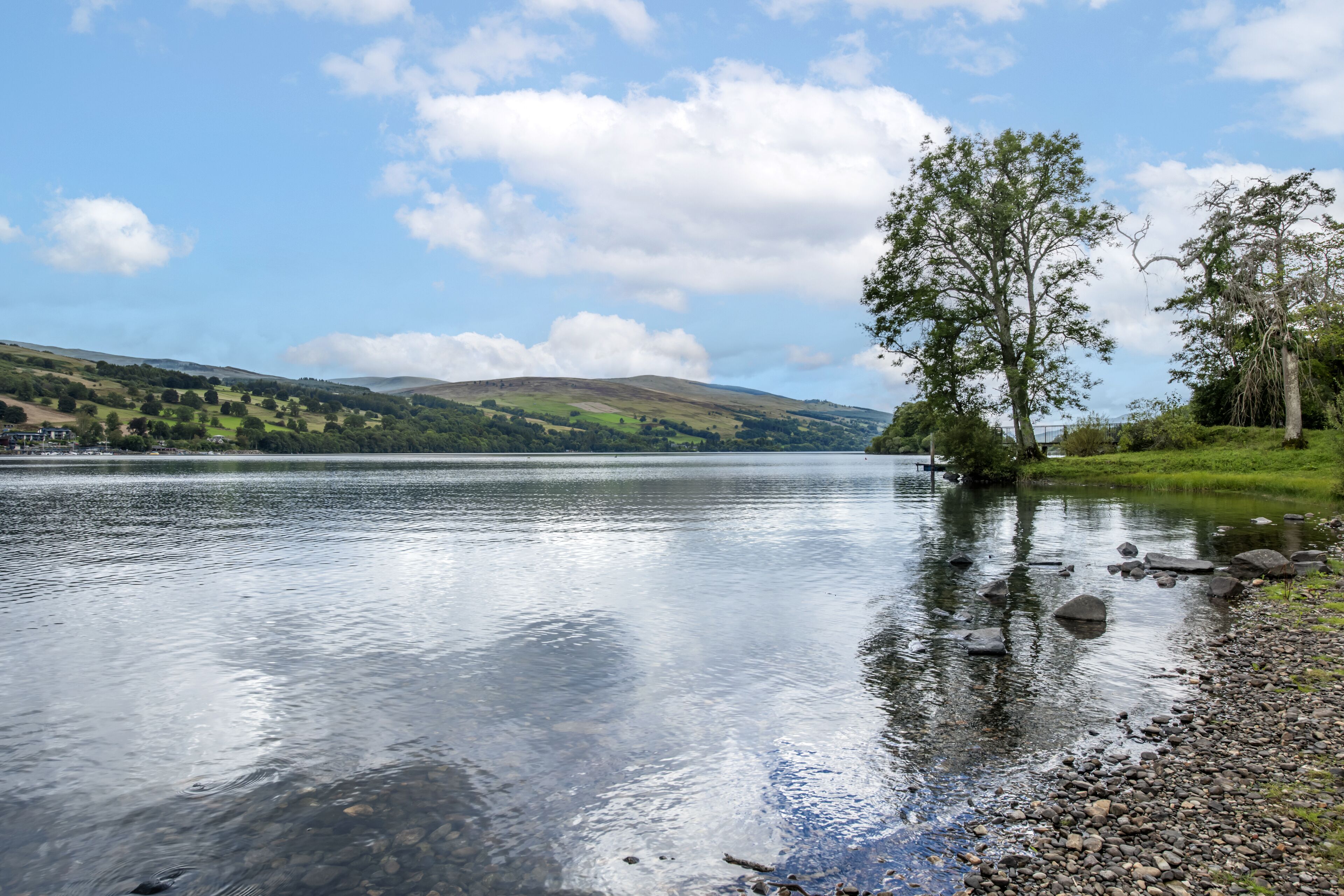 Ein ruhiger See mit klarem Wasser, umgeben von grünen Hügeln und Bäumen.