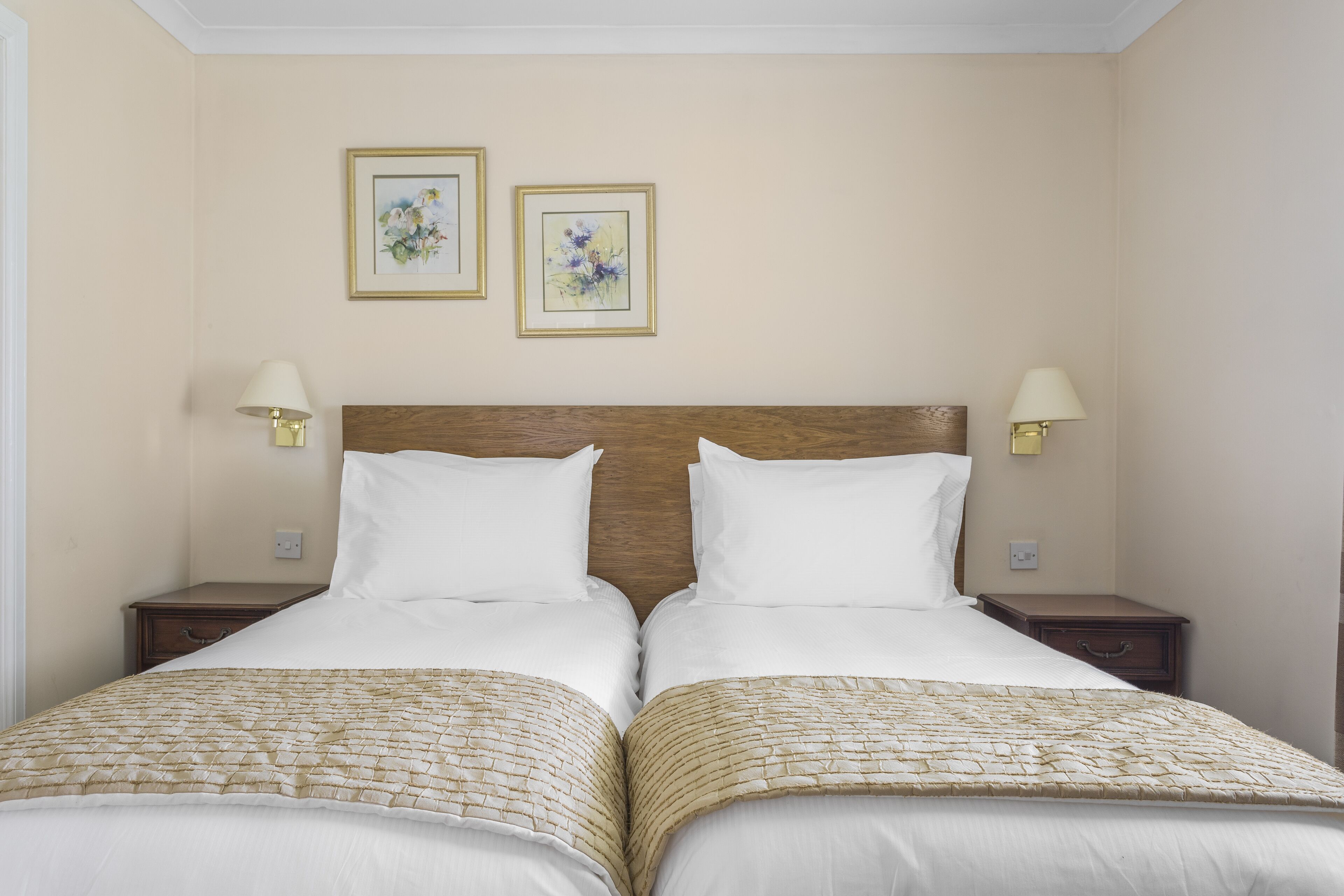 A double bed with a wooden headboard, two bedside tables with lamps, and two framed floral paintings on the wall.
