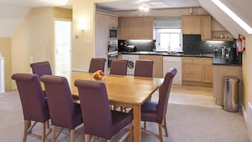 Un coin repas avec une table en bois et des chaises violettes, une cuisine avec des meubles et des appareils électroménagers en bois, et un extincteur visible.