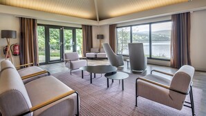 A spacious room with a high ceiling, large windows, and a view of a lake. There are several sofas and chairs arranged for seating. - The Kenmore Club (Aberfeldy)