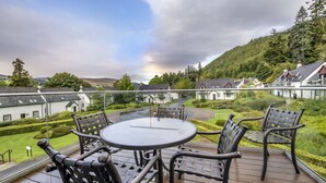 A deck with a round table and four chairs, overlooking a residential area with houses and a hill. - The Kenmore Club (Aberfeldy)