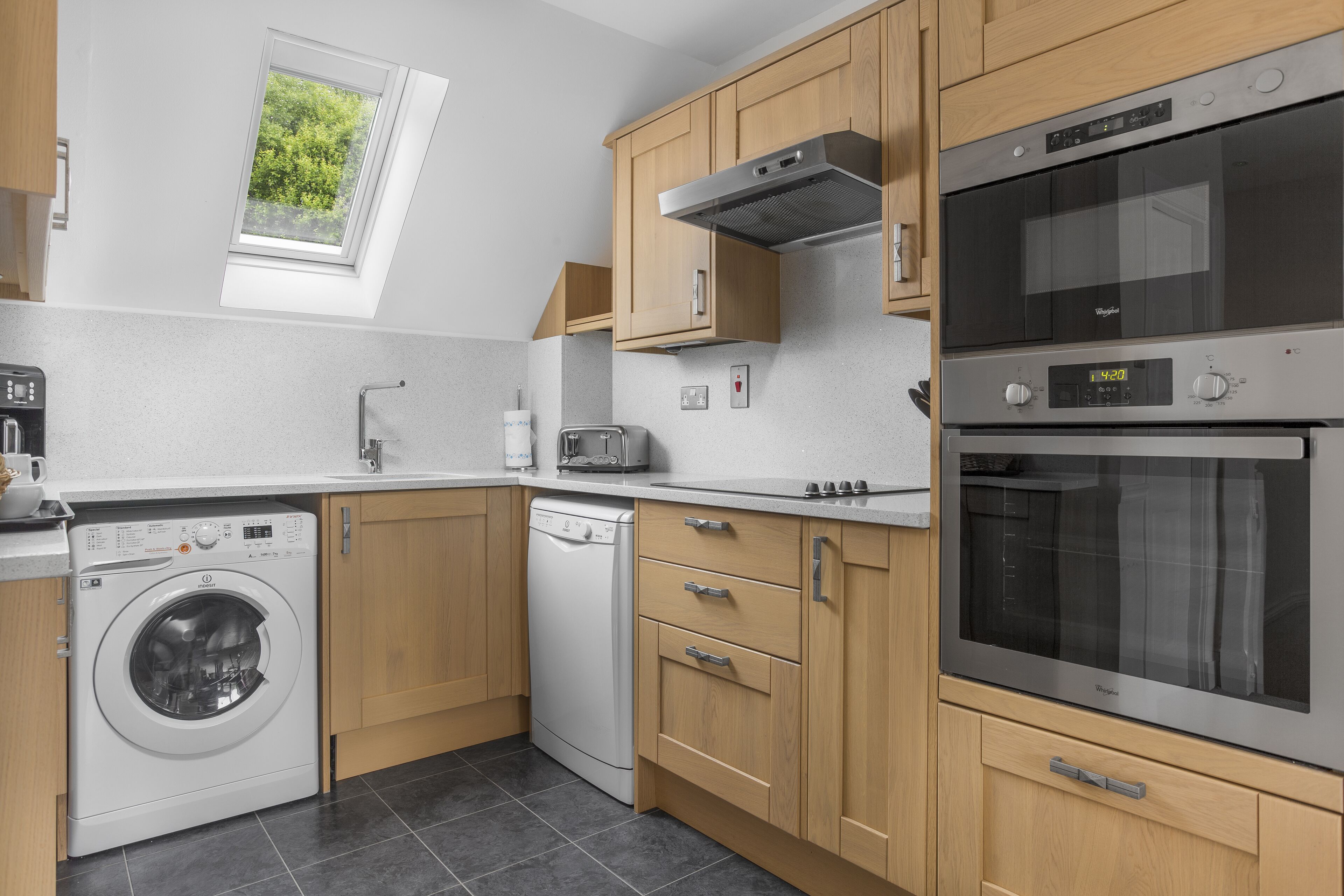 A modern kitchen with a built-in washer, dishwasher, oven, and a skylight.