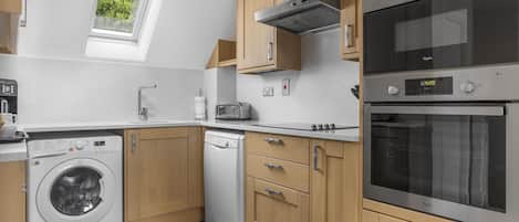 A modern kitchen with a built-in washer, dishwasher, oven, and a skylight.
