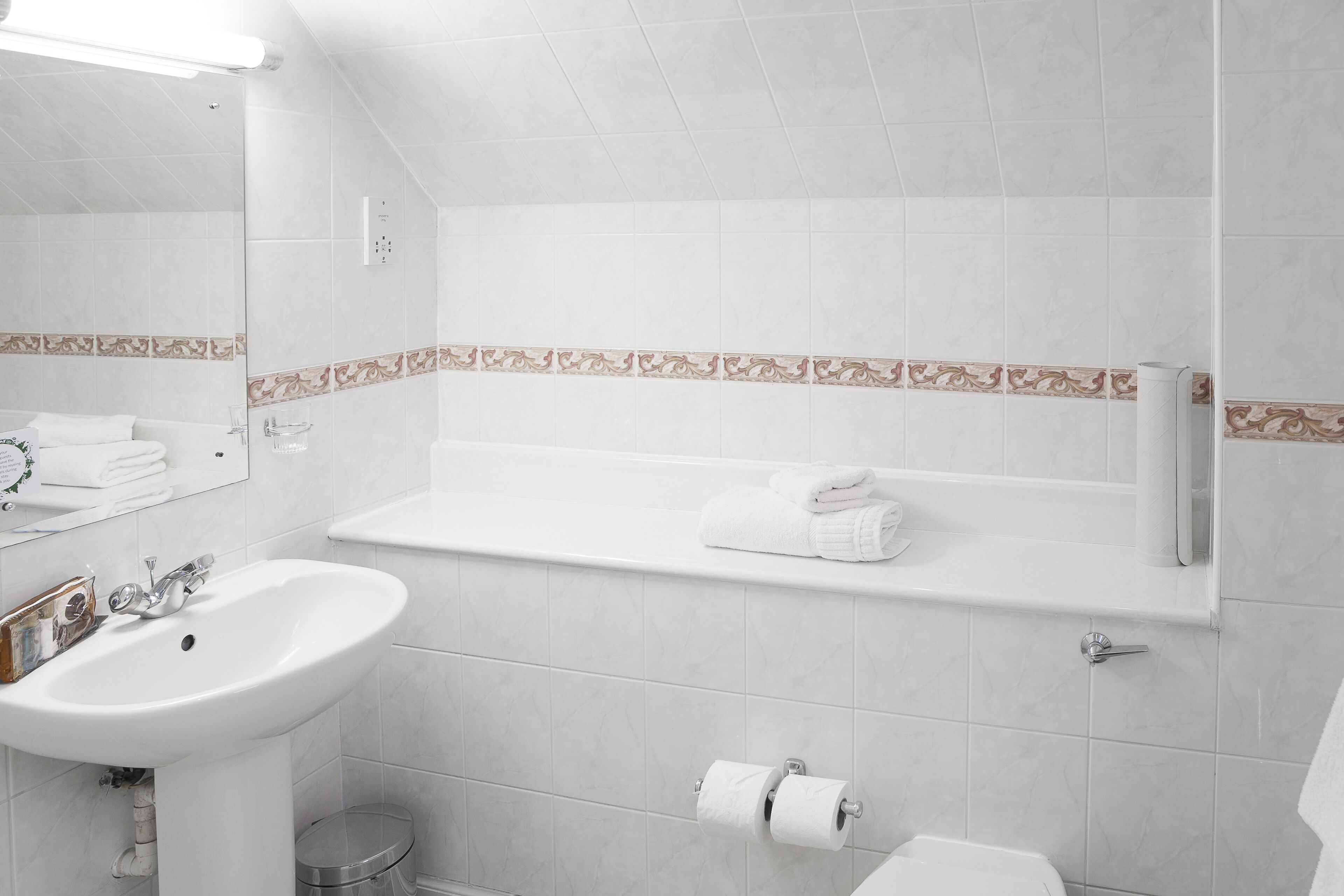 A modern bathroom with a white sink, mirror, and toilet. There is a towel rack above the toilet and a shelf with a towel.